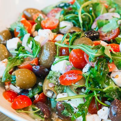 Salad, with arugula, cherry tomatoes, olives, cucumber, cheese, and olive oil.