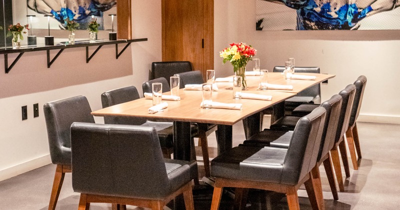 A contemporary dining room with a wooden table, black leather chairs, artwork on the wall