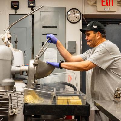 Kitchen staff member grinding cheese using an industrial grinder.