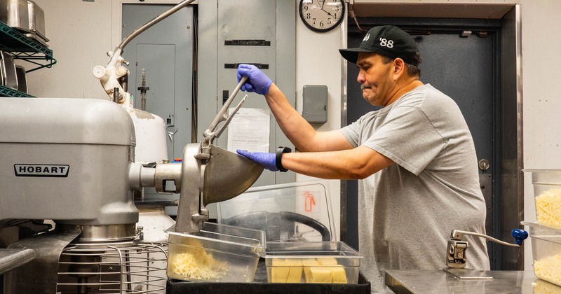 Kitchen staff member grinding cheese using an industrial grinder