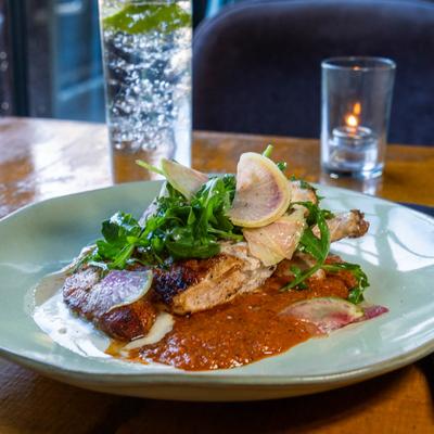 Roast chicken with arugula, radish, and sauce on a plate.