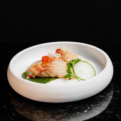 A white plate holds a piece of nigiri on a dark granite table.