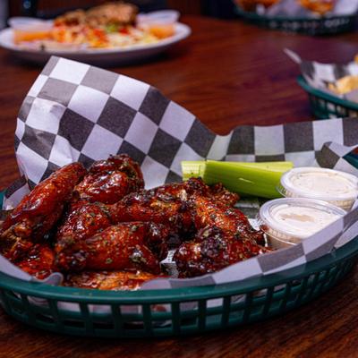 A basket of glazed chicken wings with celery sticks and dipping sauces.