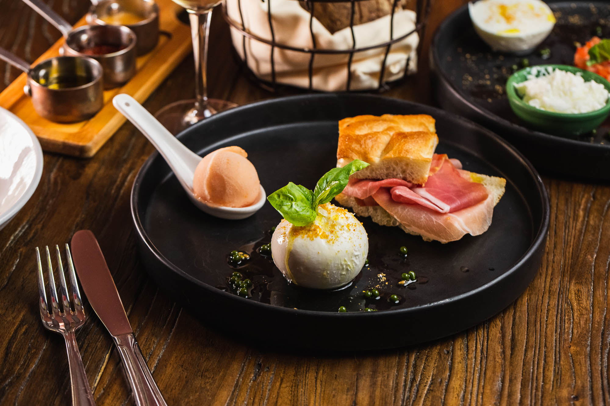 Burrata served with prosciutto, bread, and  sorbet on a spoon