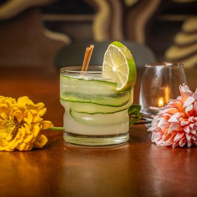 Sake Cooler cocktail with flowers and a lit candle on a wooden table.
