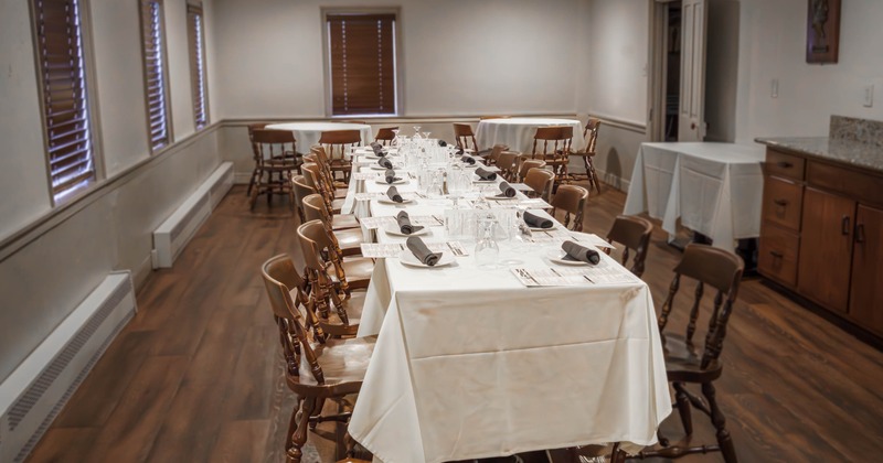 A dining area set for a formal event with a long table, white tablecloth and wooden chairs