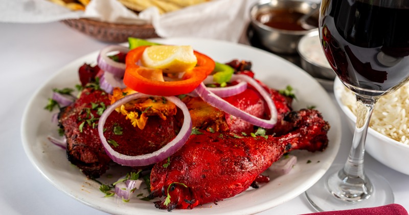 Tandoori Roasted Bone in Chicken on a white plate, next to a glass of red wine