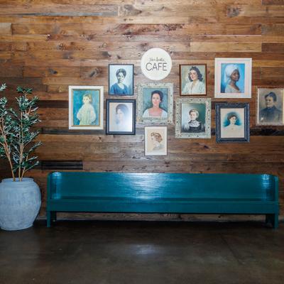 Wood-paneled cafe wall with framed portraits and teal bench.
