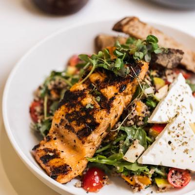 Grilled salmon salad with arugula, cherry tomatoes, quinoa, and feta cheese.
