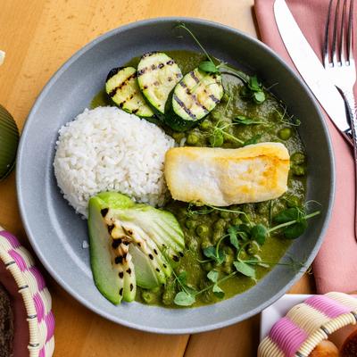 Grilled white fish with rice, zucchini, and green pea sauce on a gray plate.