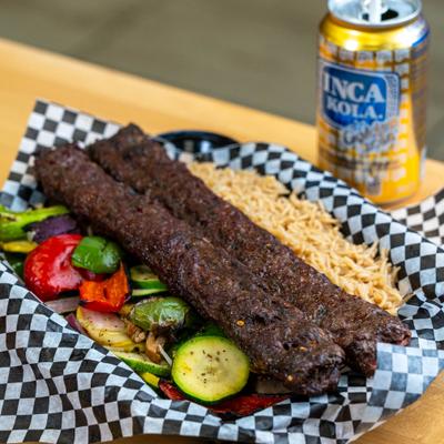 Grilled beef shish kebabs with vegetables and rice served beside a can of Inca Kola.