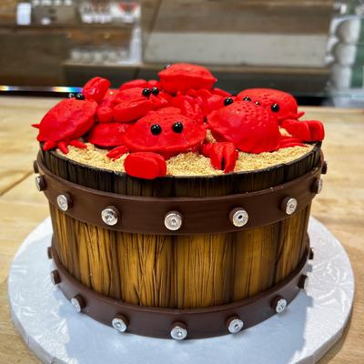 A cake designed like a wooden barrel, topped with red fondant crabs on sandy crumbs.