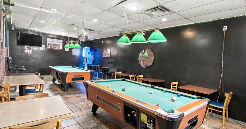 Game room with pool tables, seating, and green pendant lights