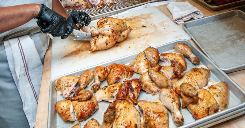 Kitchen, staff cutting roasted whole chicken into pieces