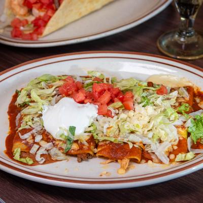 Enchiladas topped with enchilada sauce, cheese, lettuce, tomato, and sour cream.