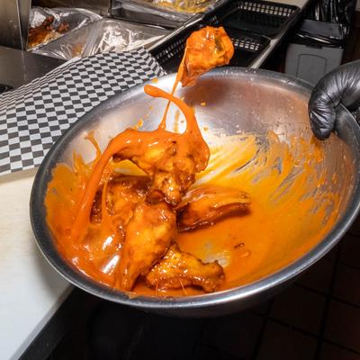 Action shot of chicken wings getting covered in a sauce.