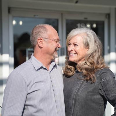 The owners standing in front of the restaurant, smiling and looking into each other's eyes.