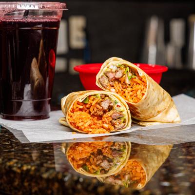 Steak Burrito sliced in half and served alongside a drink in a plastic cup.