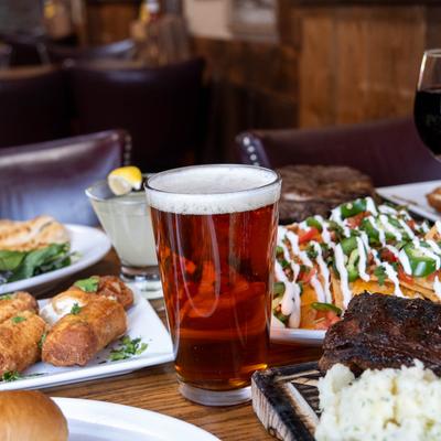 A pint of beer surrounded by plates of food and other drinks.