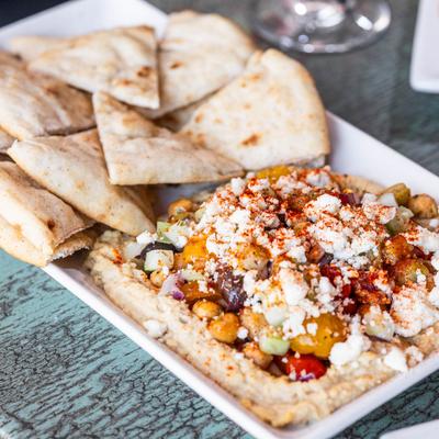 Hummus loaded with olives, tomatoes, feta, cucumber, onion, and chickpeas, pita on the side.