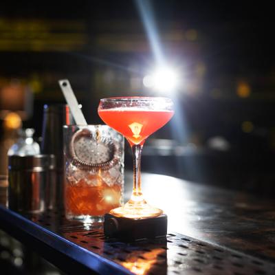A vibrant cocktail in a delicate glass is spotlighted on a dimly lit bar counter,.