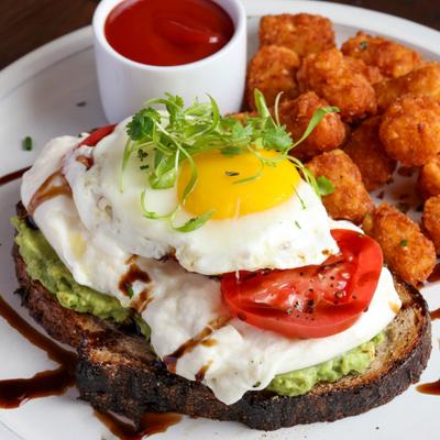 Avocado toast topped with fried egg, tomatoes, microgreens, and  served with tater tots.
