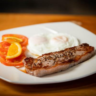 Bisteak and fried egg with tomato garnish.