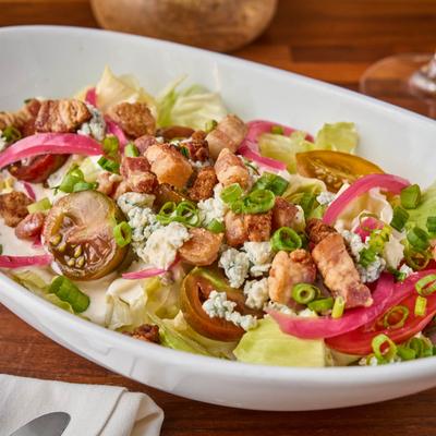 Iceberg Wedge Salad, with lettuce, pickled red onion, bacon, blue cheese, and scallions.