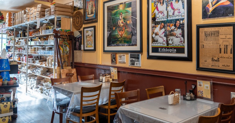 Interior with shelves filled with food products, decorated walls featuring colorful artwork, and wooden tables and chairs