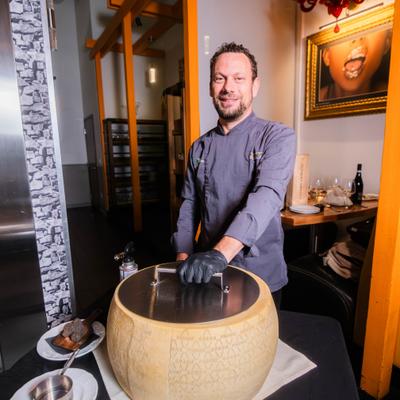 Chef standing behind a cheese wheel in a restaurant.
