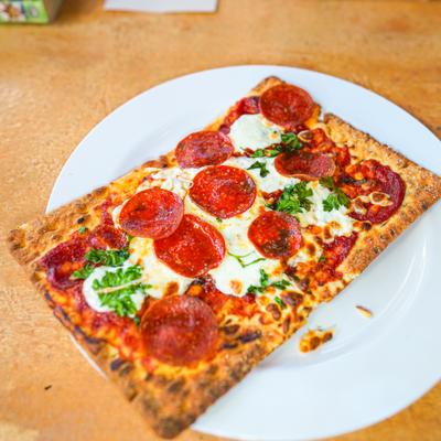 Rectangular pepperoni pizza on white plate atop a wooden table.