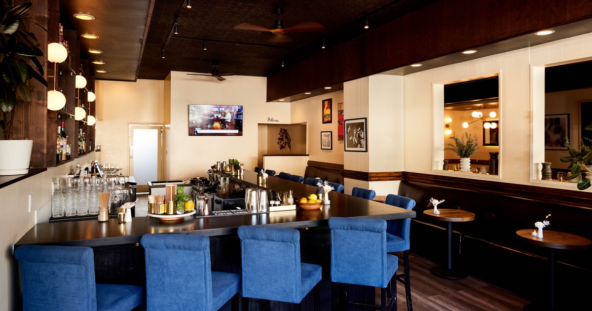 Modern bar interior with blue chairs, dark wooden bar, pendant lights, and decorative ceiling