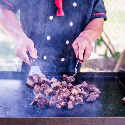 Chef grilling meat outdoors with smoke rising.
