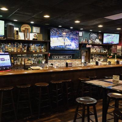 Bar area with a counter, stools, well-stocked bar shelves and television screens.