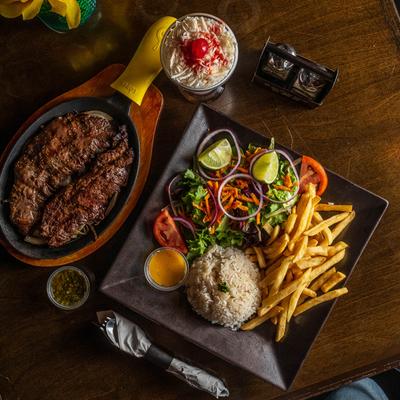 Beef steak  served with mixed salad ,fries, rice, sauces, and a dessert, top view.