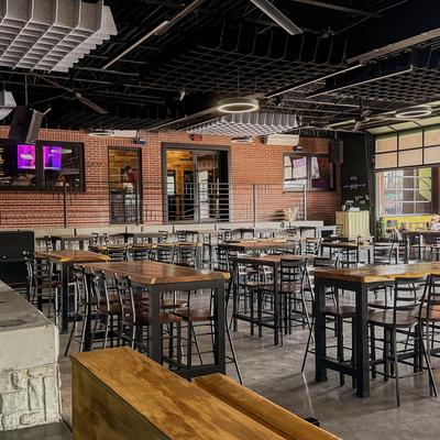 Dining area with high tables, brick walls, and black ceiling structures.