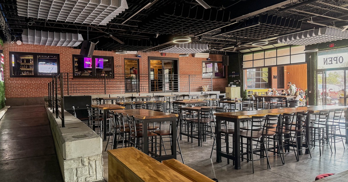 Interior of a modern industrial-style restaurant with high-top tables, bar stools, and brick walls