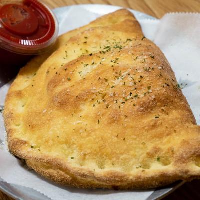 Calzone topped with herbs and served alongside a small container of marinara sauce.