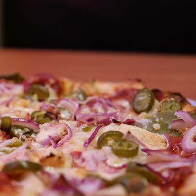 Closeup of pizza with pepperoni, jalapenos, pineapples, garlic, red onions, and cilantro.