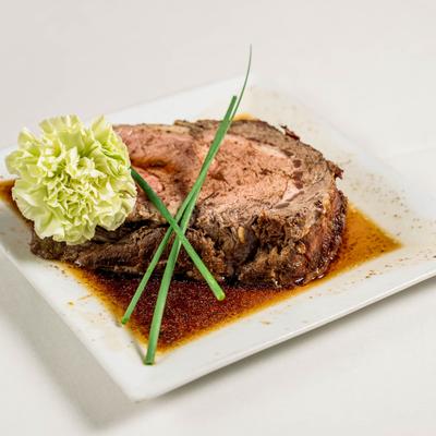 Prime rib roast served in au jus with chives on a white plate.
