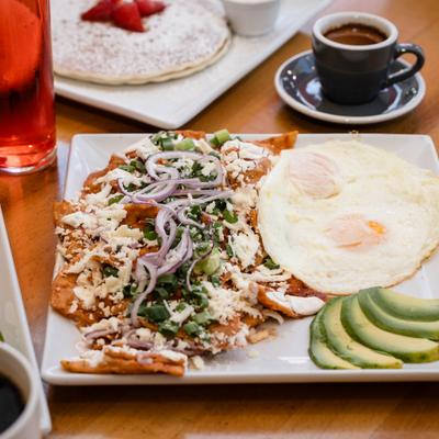 Chilaquiles platter with fried eggs and avocado slices beside a cup of coffee.