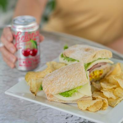 Sandwich on a white plate served with potato chips and a canned drink.
