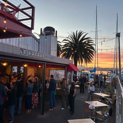 People socializing outside the restaurant by the marina at sunset.