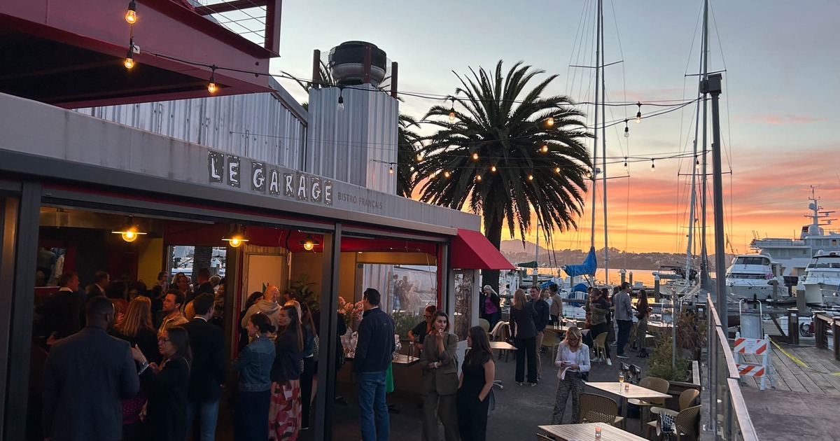 People socializing outside the restaurant by the marina at sunset