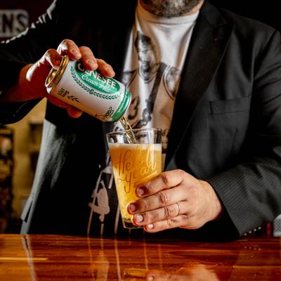 A person pouring a can of ale into a glass at a table.