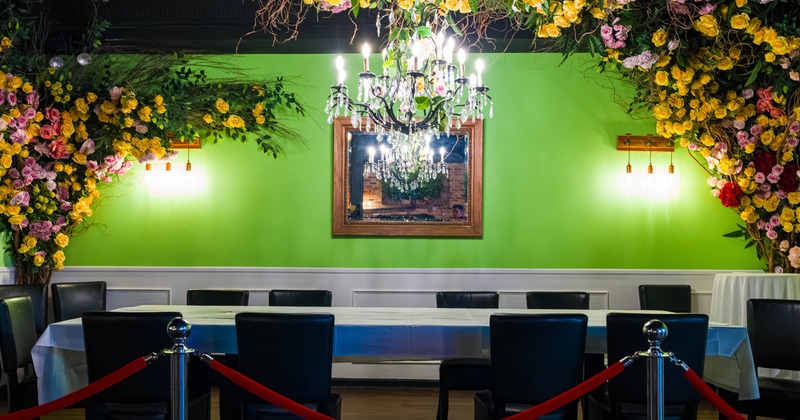 A decorative dining area - a chandelier, floral arrangements and a long table with black chairs