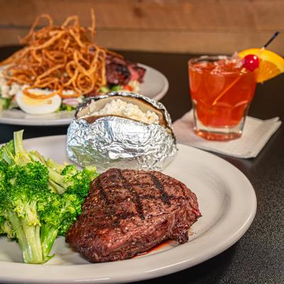 Sirloin steak served with broccoli and baked potato, alonside a cocktail.