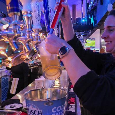A bartender pouring a glass of beer from a tap.
