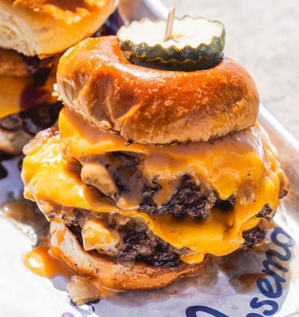 A double cheeseburger with melted cheddar, pickles on top, and a toasted bun