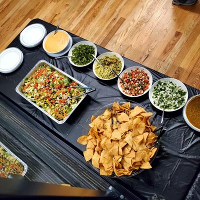 Catering setup featuring a central bowl of tortilla chips surrounded by various toppings.